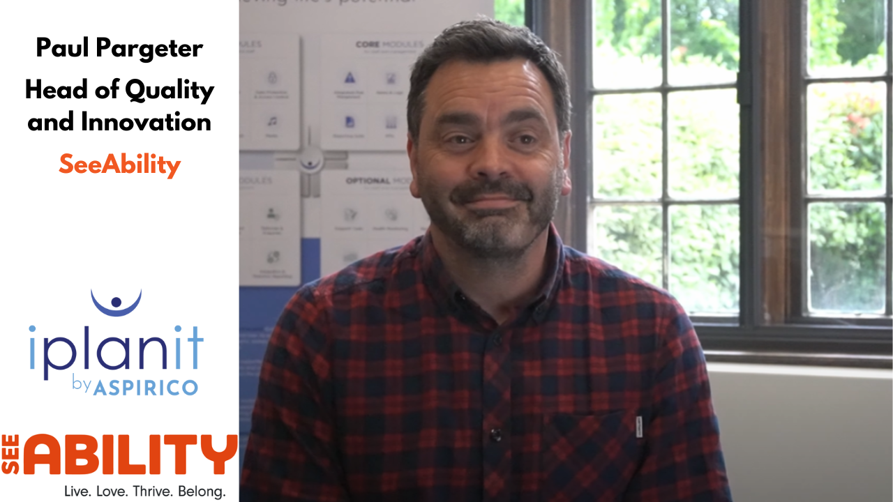 A man in a red and black checkered shirt sits indoors in front of a window. Text on the image reads, 